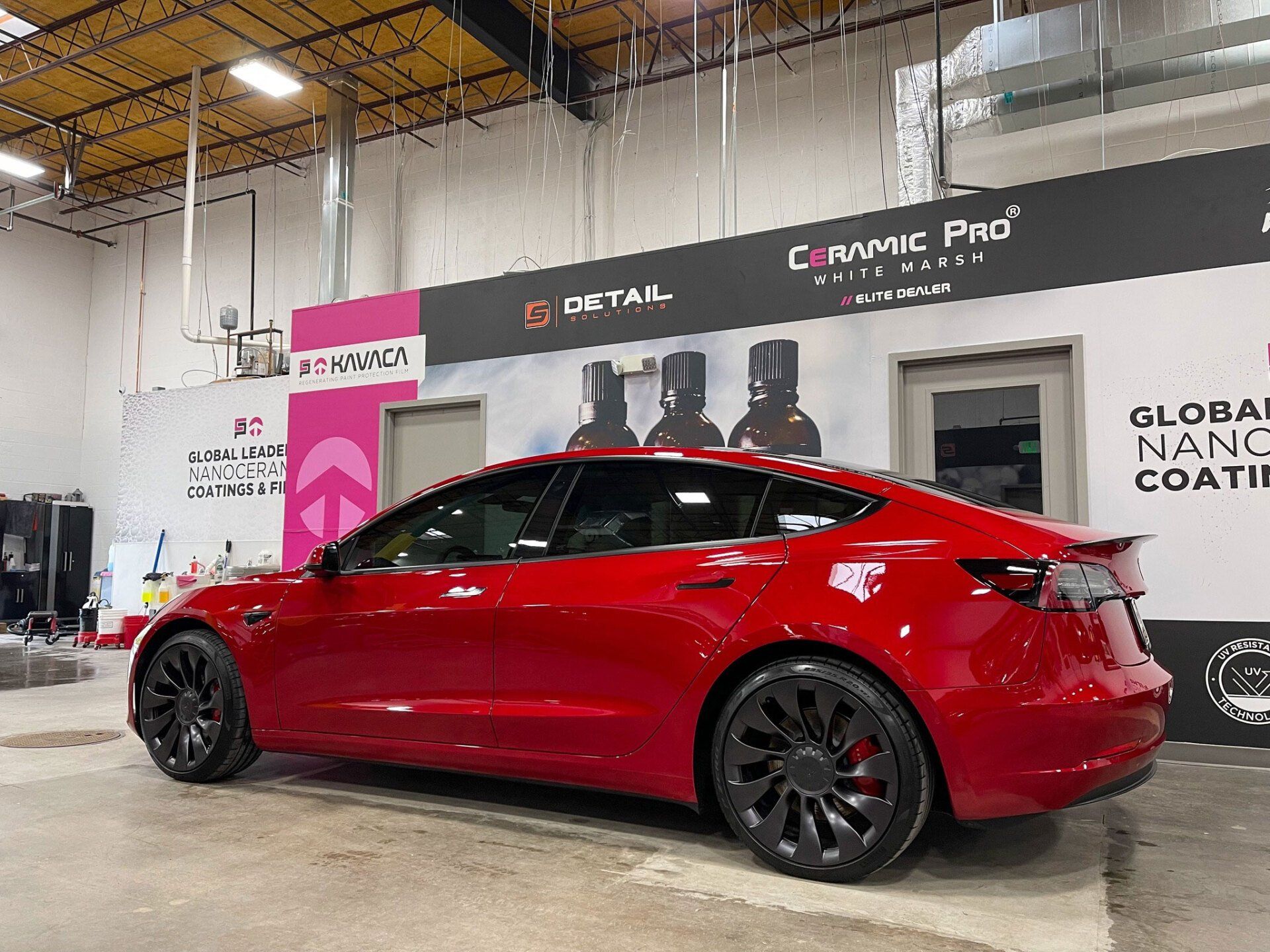 A red tesla model 3 is parked in a garage.