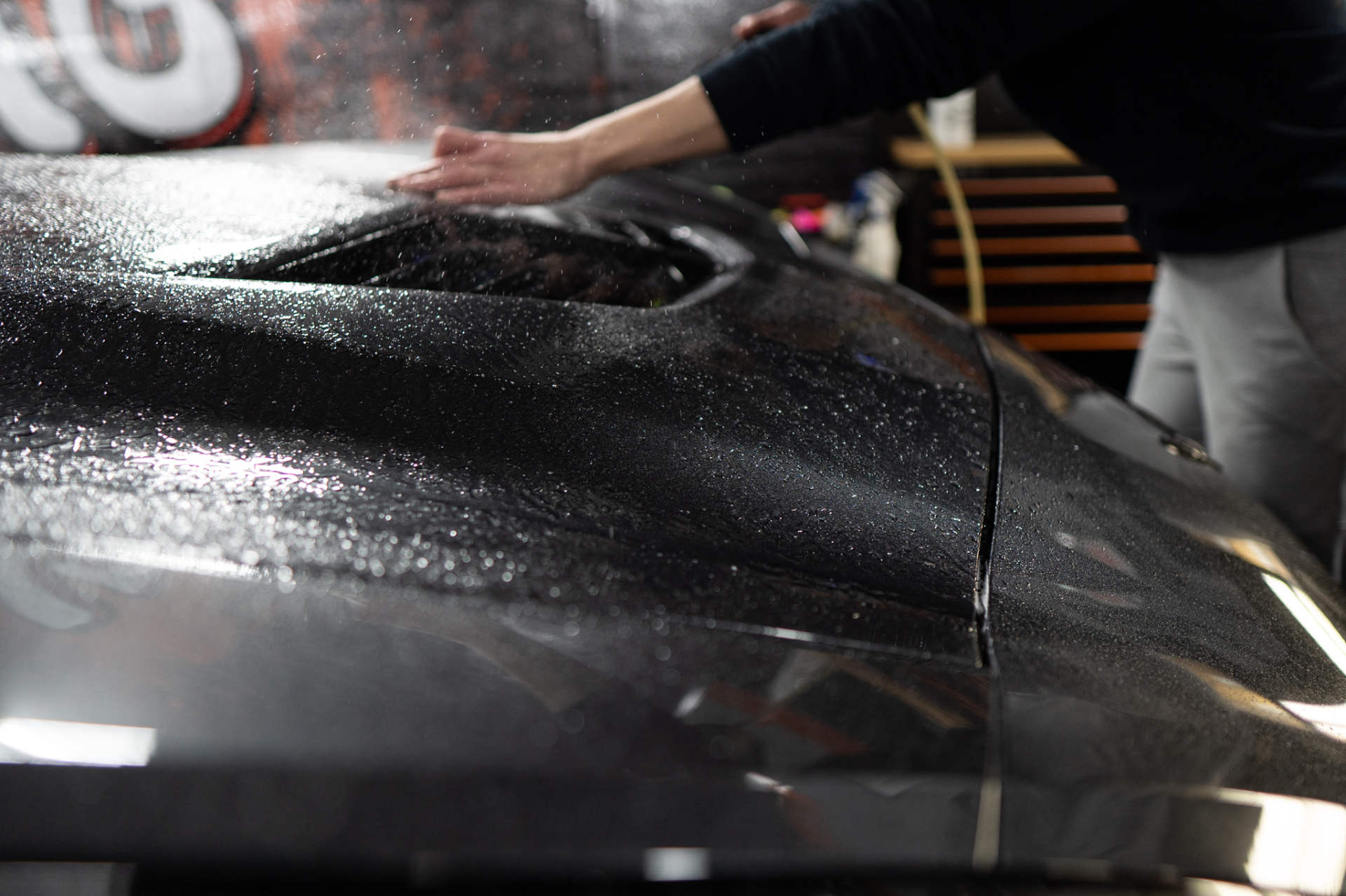 A person is spraying water on the hood of a car.