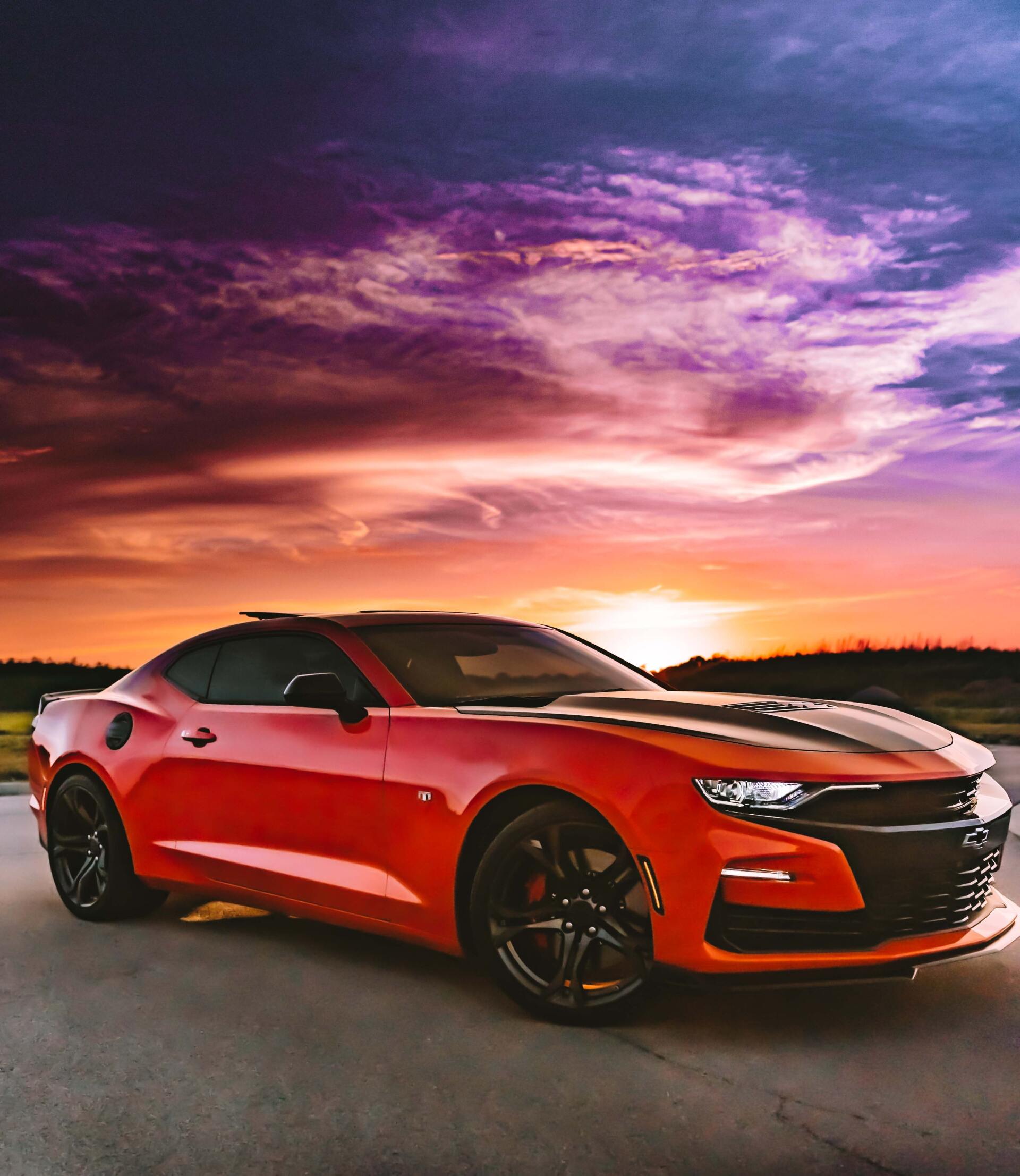 A red sports car is parked on the side of the road at sunset.