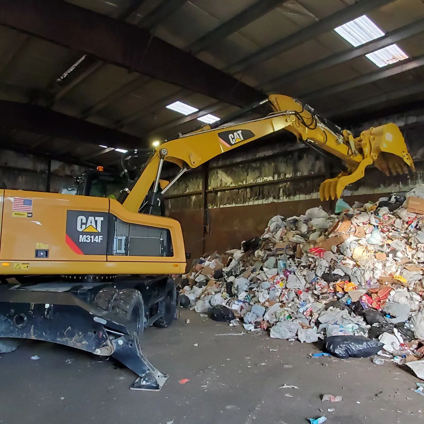 Yellow CAT excavator loading trash inside a waste facility.
