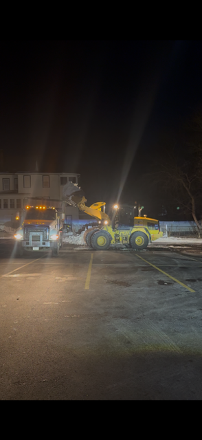 Tow truck and fire truck at night on a road with flashing lights, beside a snowbank and trees