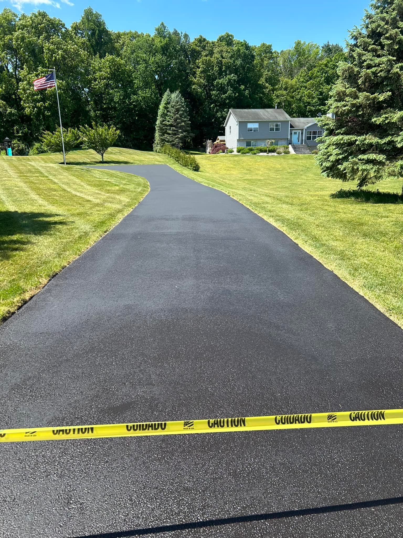 A person is using a broom to spread asphalt on a driveway.