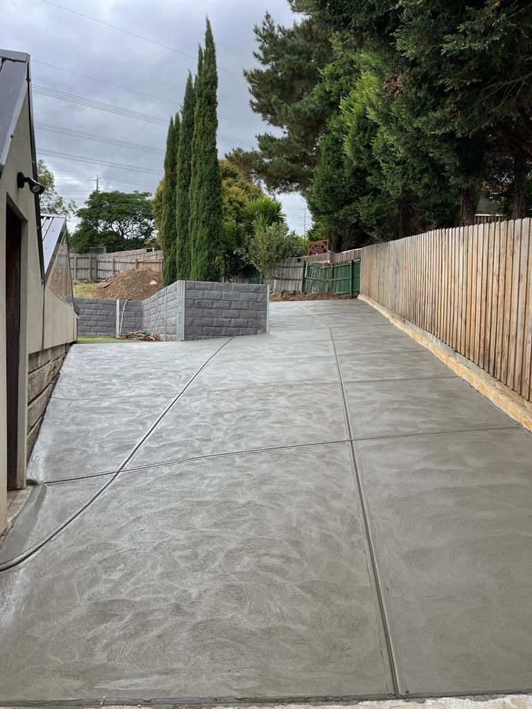 A concrete driveway leading up to a house with trees on the side.