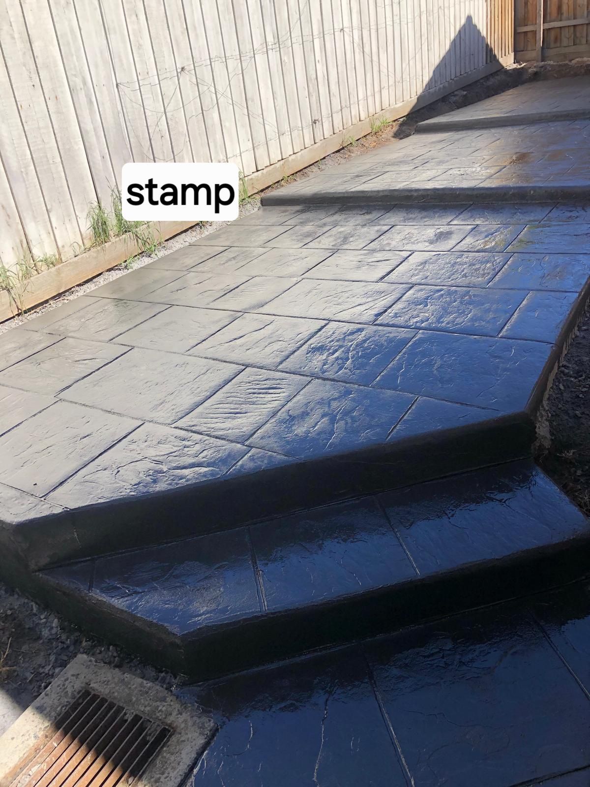 A stamped concrete driveway with steps and a fence in the background.