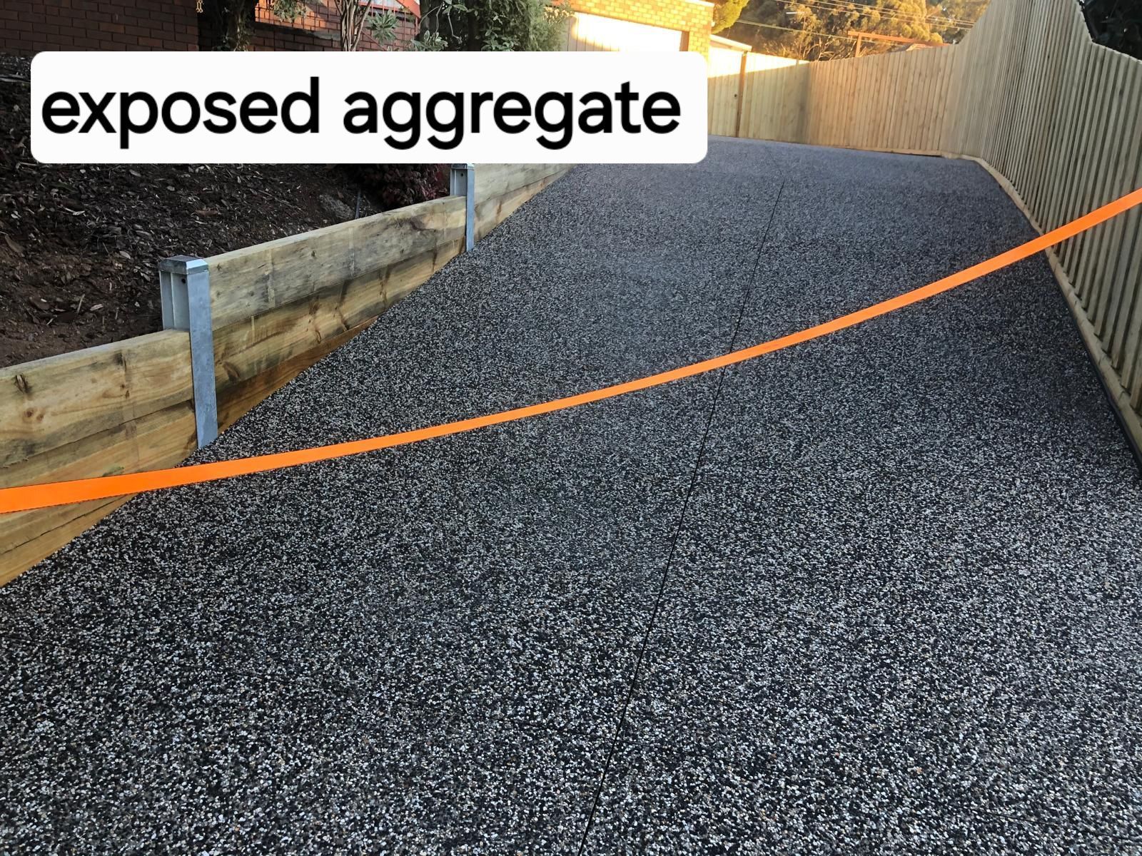 An exposed aggregate driveway with a wooden fence in the background.
