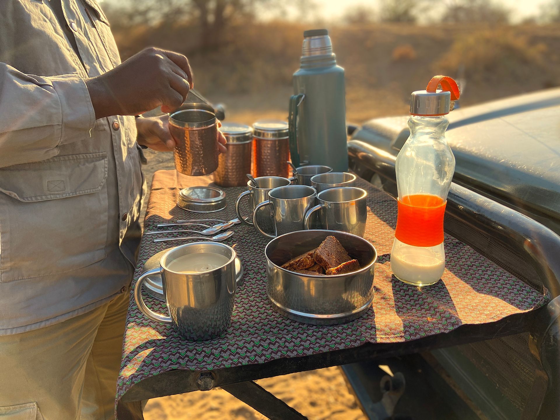 A person preparing a picnic snack on a vehicle's tailgate in a sunny, outdoor desert environment.