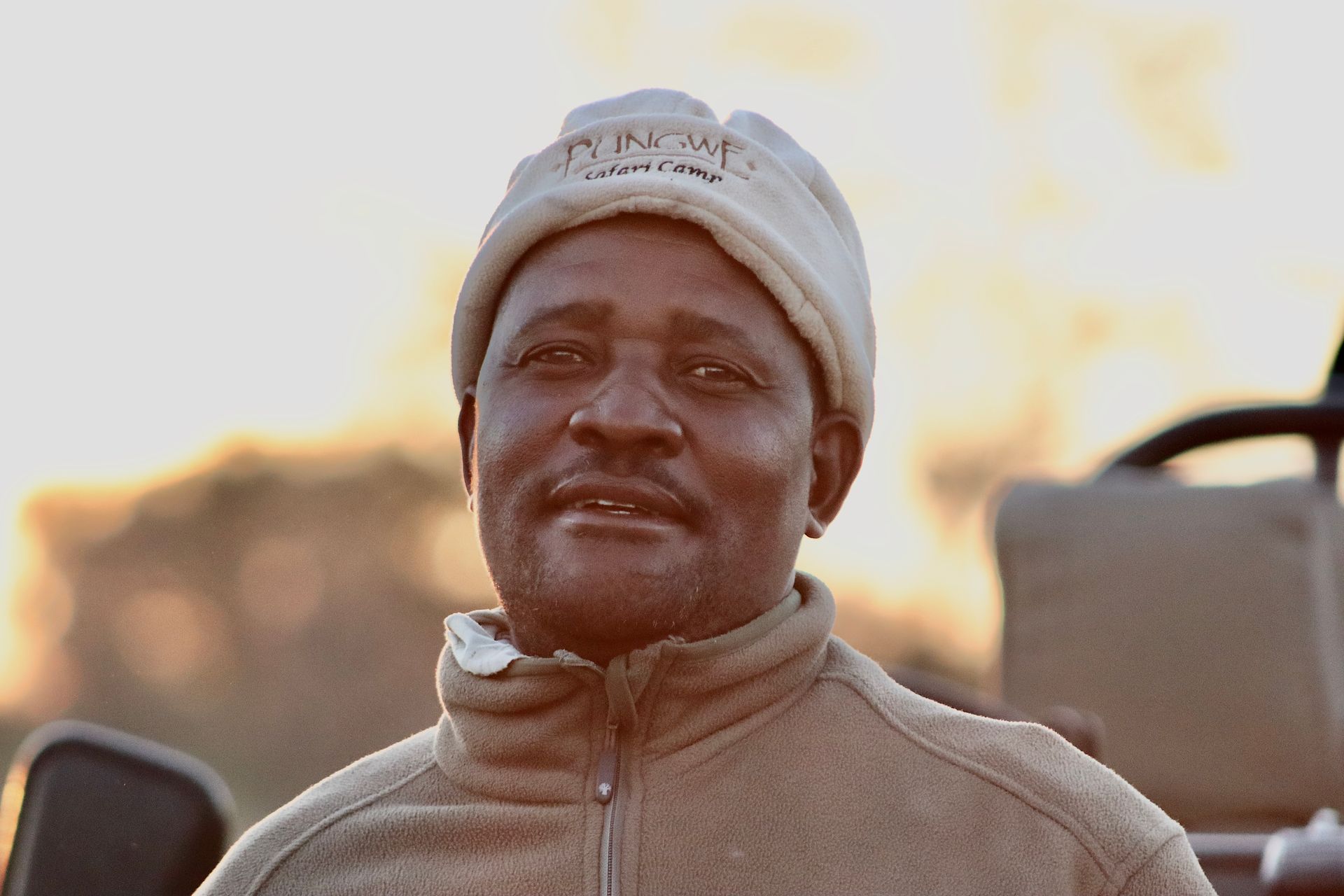 A person in a fleece jacket and beanie, looking toward the camera with a calm expression against a blurred outdoor background.