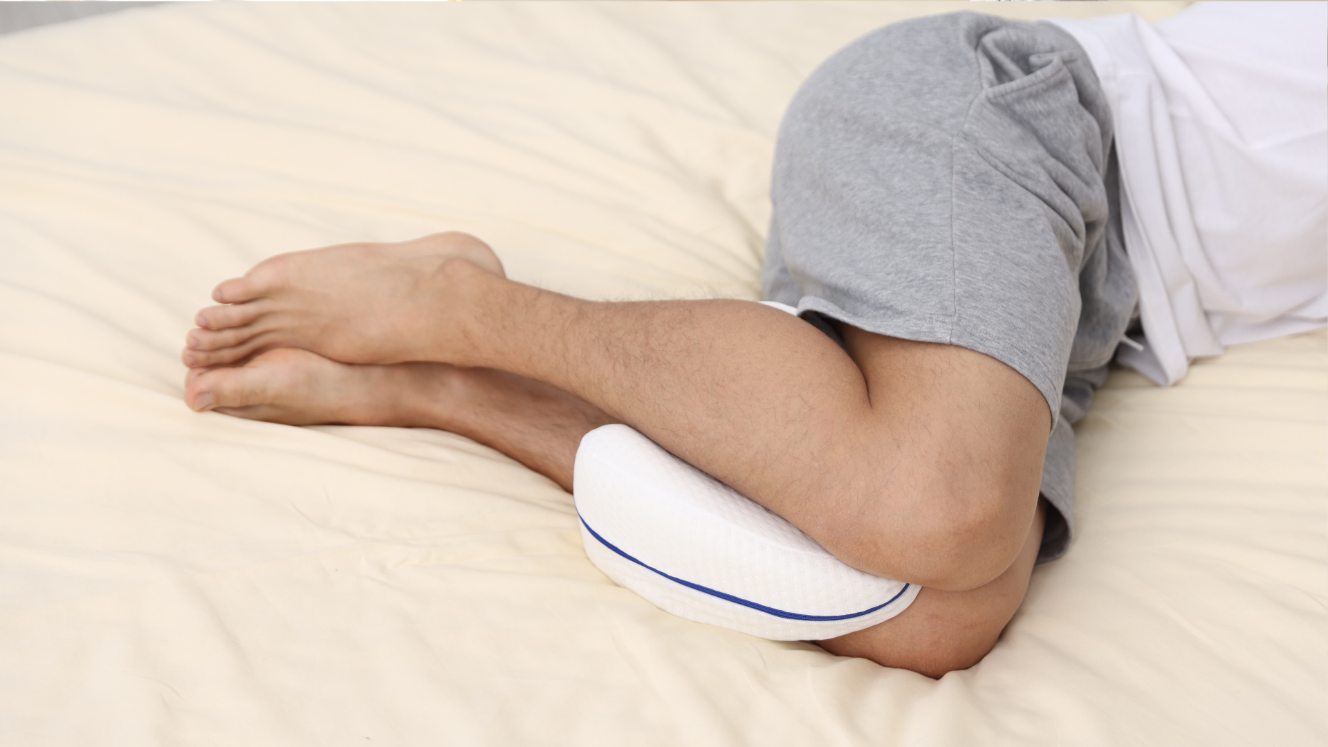 Person lying on a bed with a white knee pillow supporting bent legs.