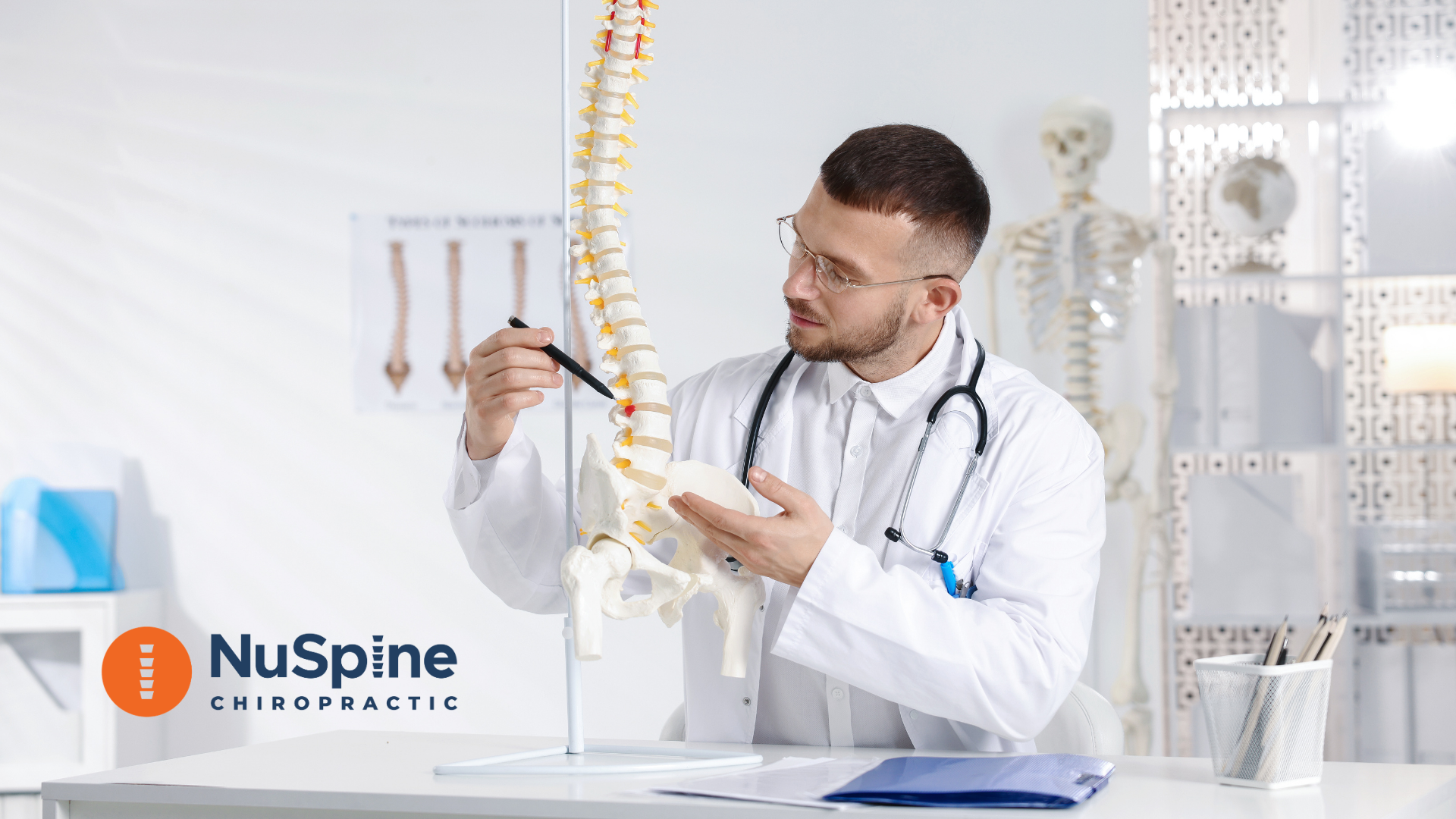 Un quiropráctico con bata blanca señalando un modelo de columna vertebral en un consultorio clínico.