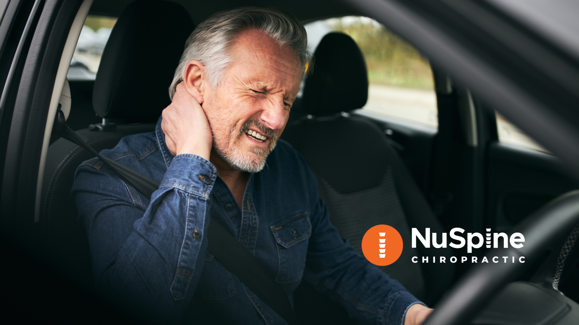 A man is sitting in a car with his hand on his neck.