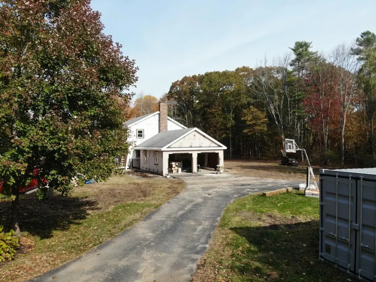 A house with a garage and a driveway is surrounded by trees.