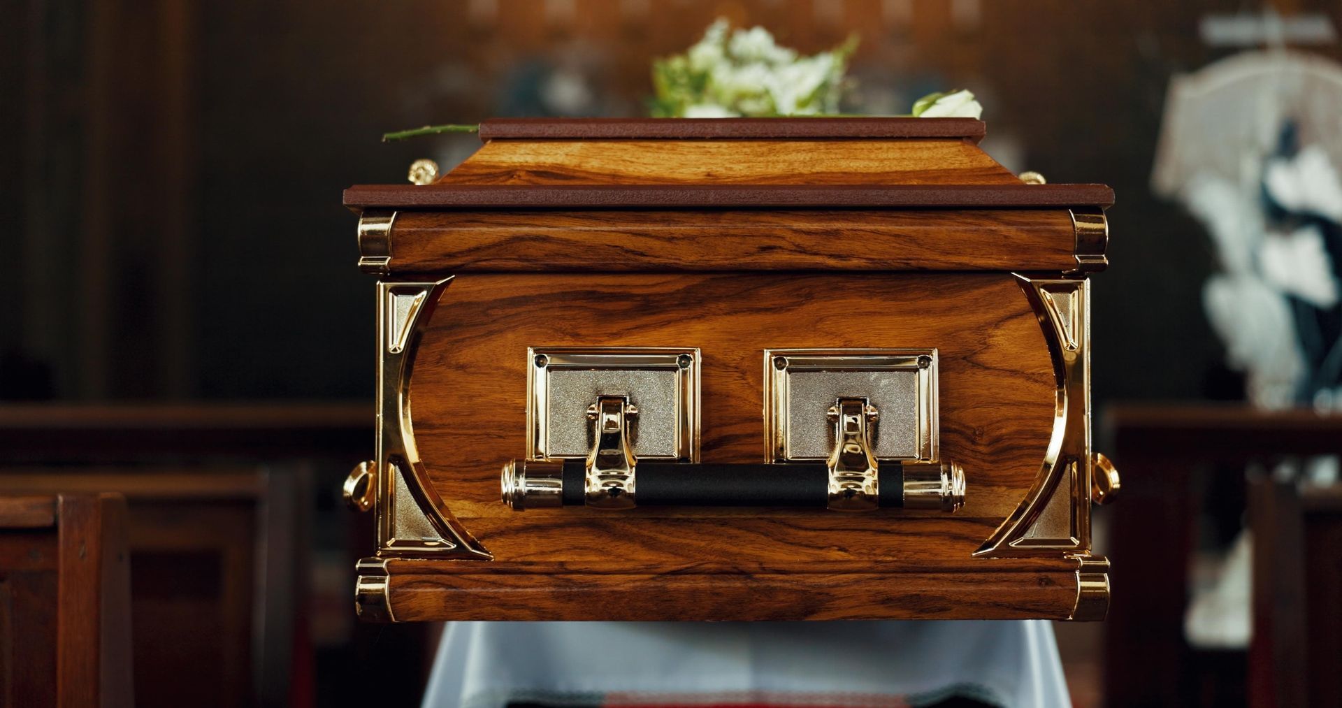 Wooden casket with gold accents and handles, inside a church.