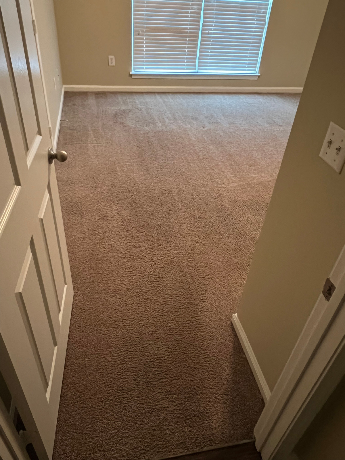 An empty room with a carpeted floor and a window.
