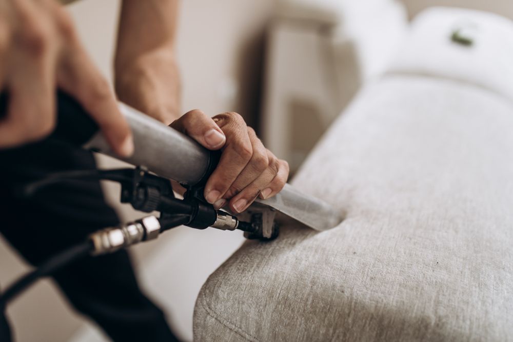 A person is cleaning a couch with a vacuum cleaner.