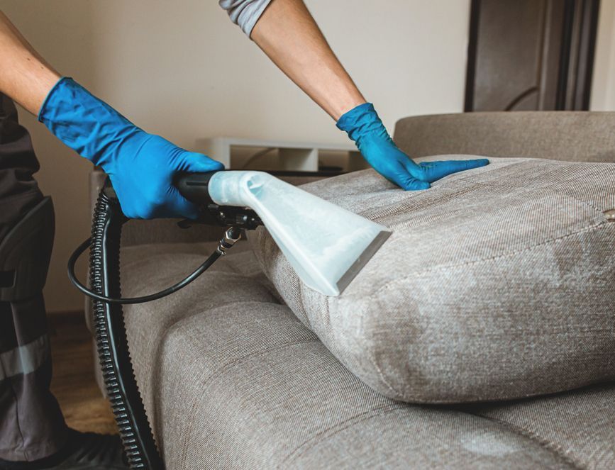 A person is cleaning a couch with a vacuum cleaner.