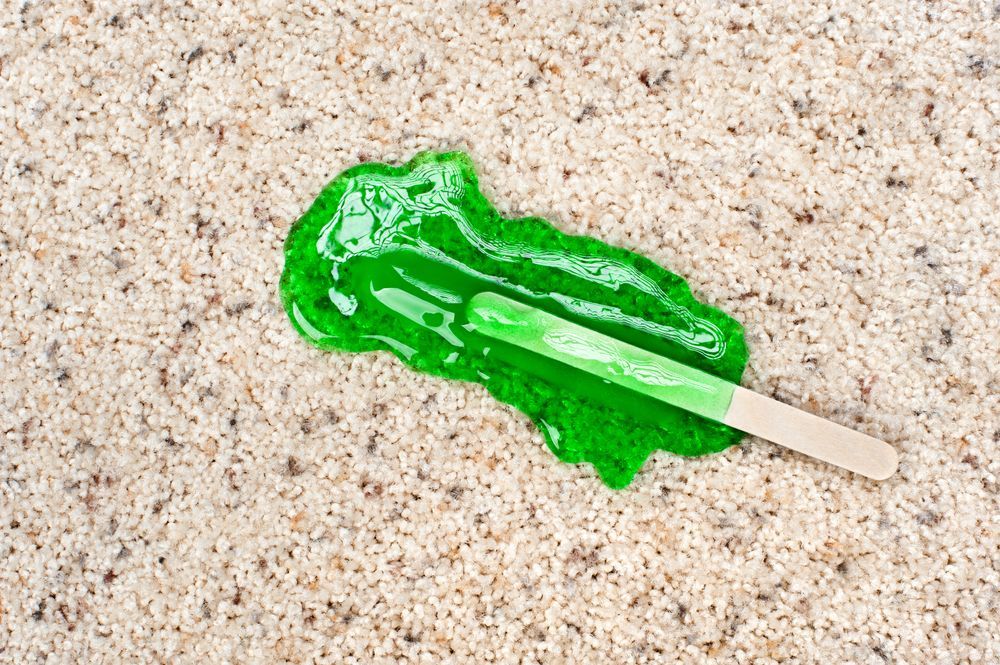 A green ice cream stick is melting on a carpet.