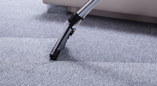 A vacuum cleaner is cleaning a carpet next to a couch.