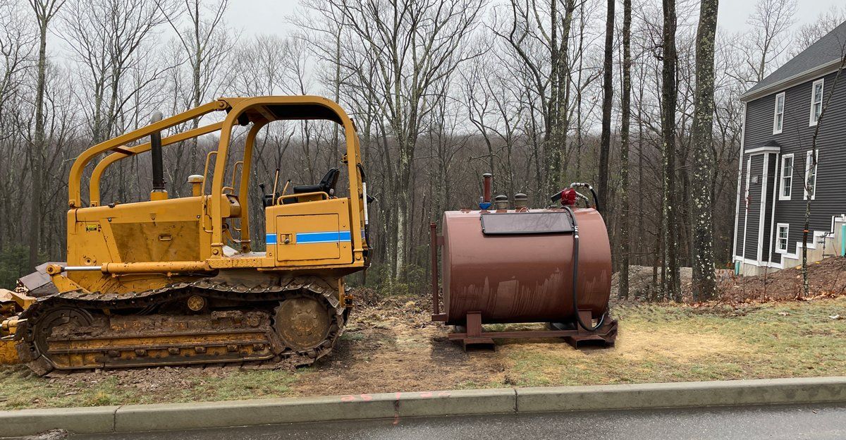 A bulldozer is parked next to a large tank on the side of the road.