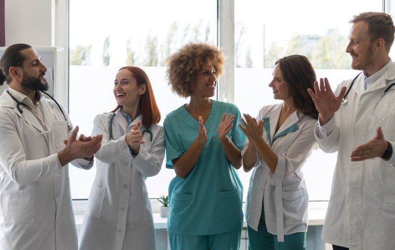 Healthcare staff in white and teal scrubs clapping together in a bright hospital room