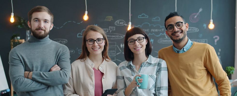 Four coworkers smiling in an office, standing in front of a chalkboard