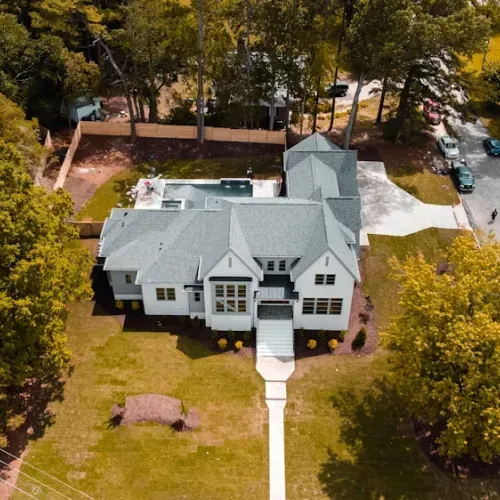 Aerial view of a large gray house with a white walkway and trees in the yard.
