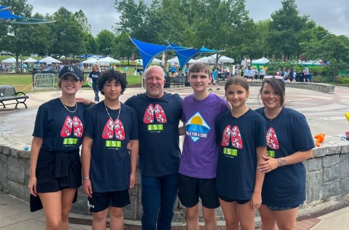 Six people standing together outdoors by a pool, smiling in matching event shirts.