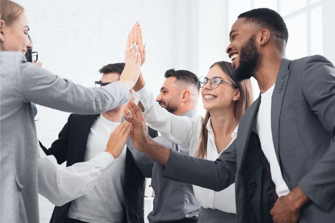 Office team high-fiving in a bright meeting room, smiling and celebrating success