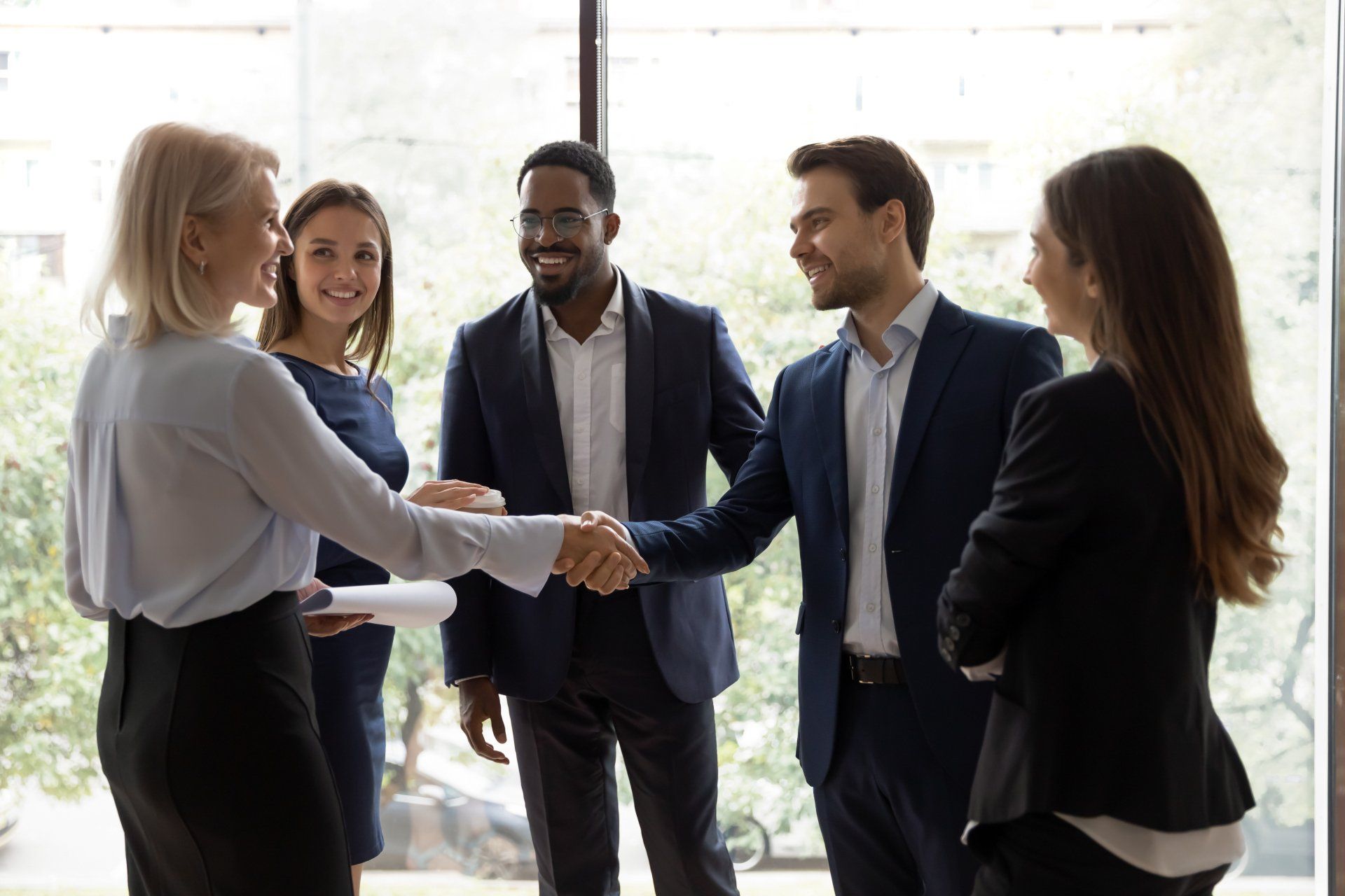 Five professionals in business attire shaking hands during a networking meeting in a bright office