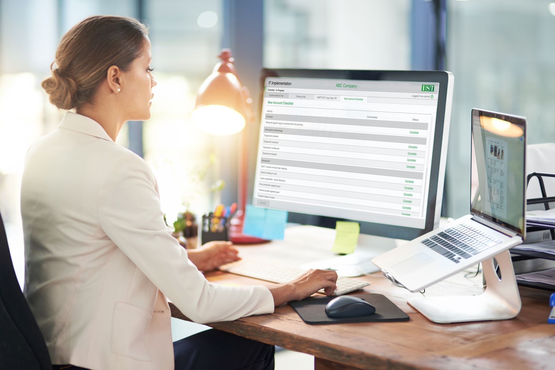 Person working at a desk with dual monitors in a bright office, using a laptop and keyboard