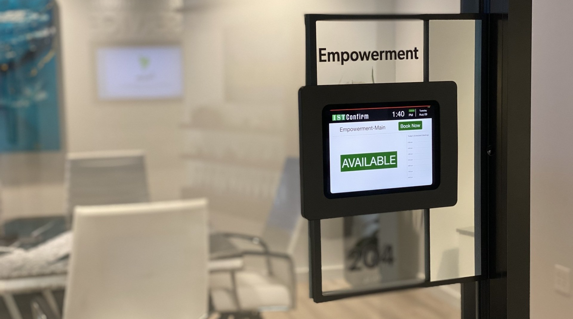 Small kiosk screen on a glass door in an office, displaying a green checkmark and “AVAILABLE” sign.
