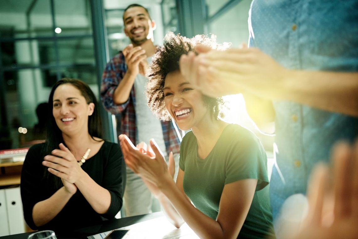People clapping in a bright office, smiling during a celebration