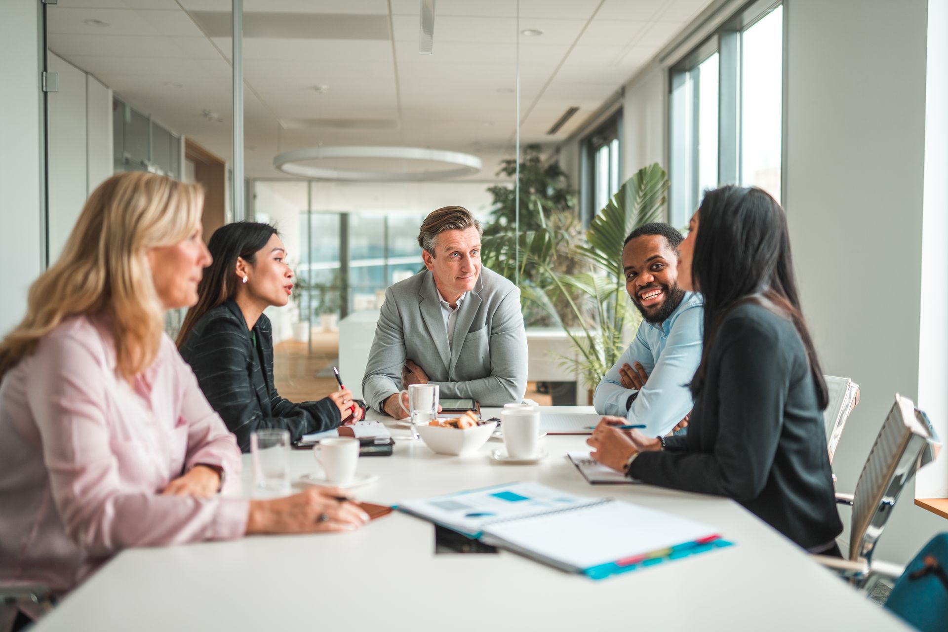 a group of five employees, diverse in age and race, discuss their roles at a table in an office