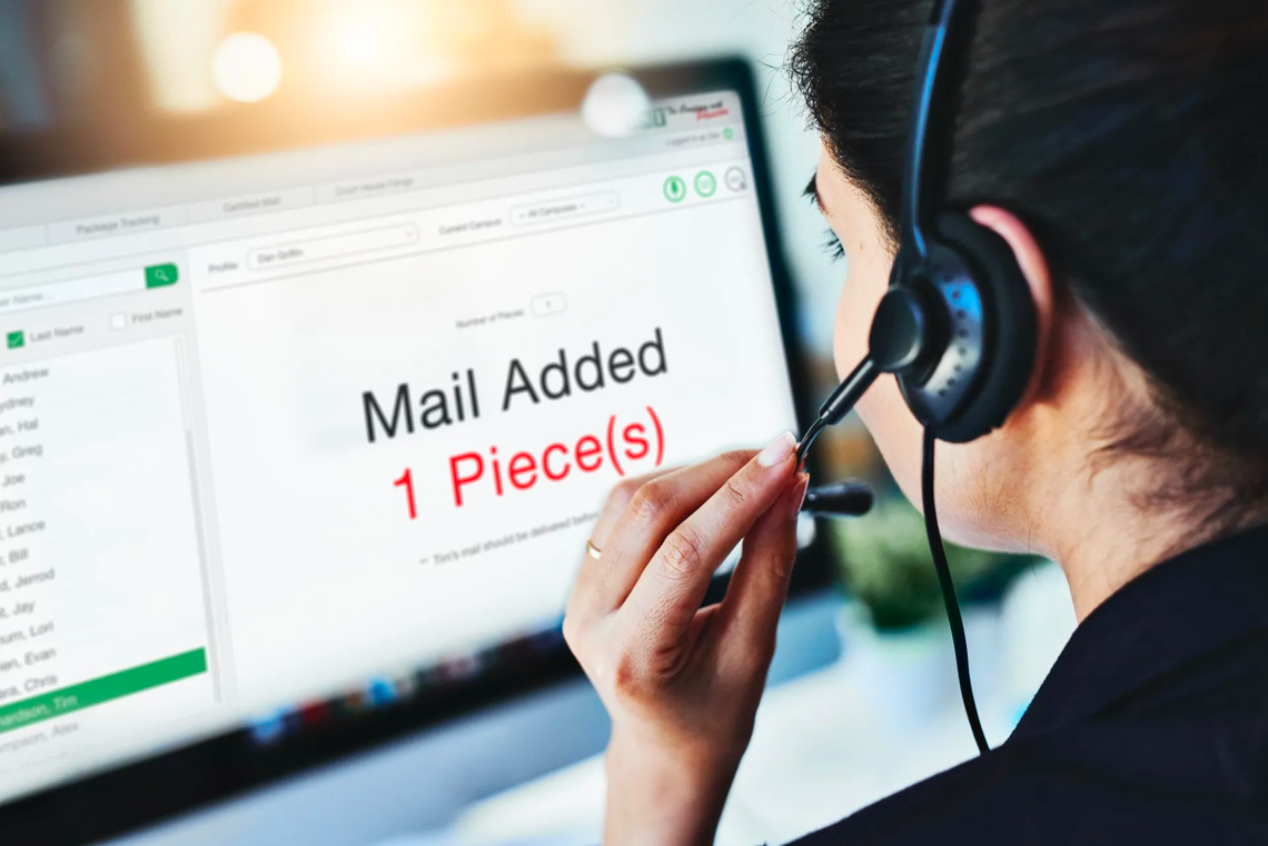 Headset-wearing worker looking at monitor with “Mail Added 1 Piece(s)” on screen