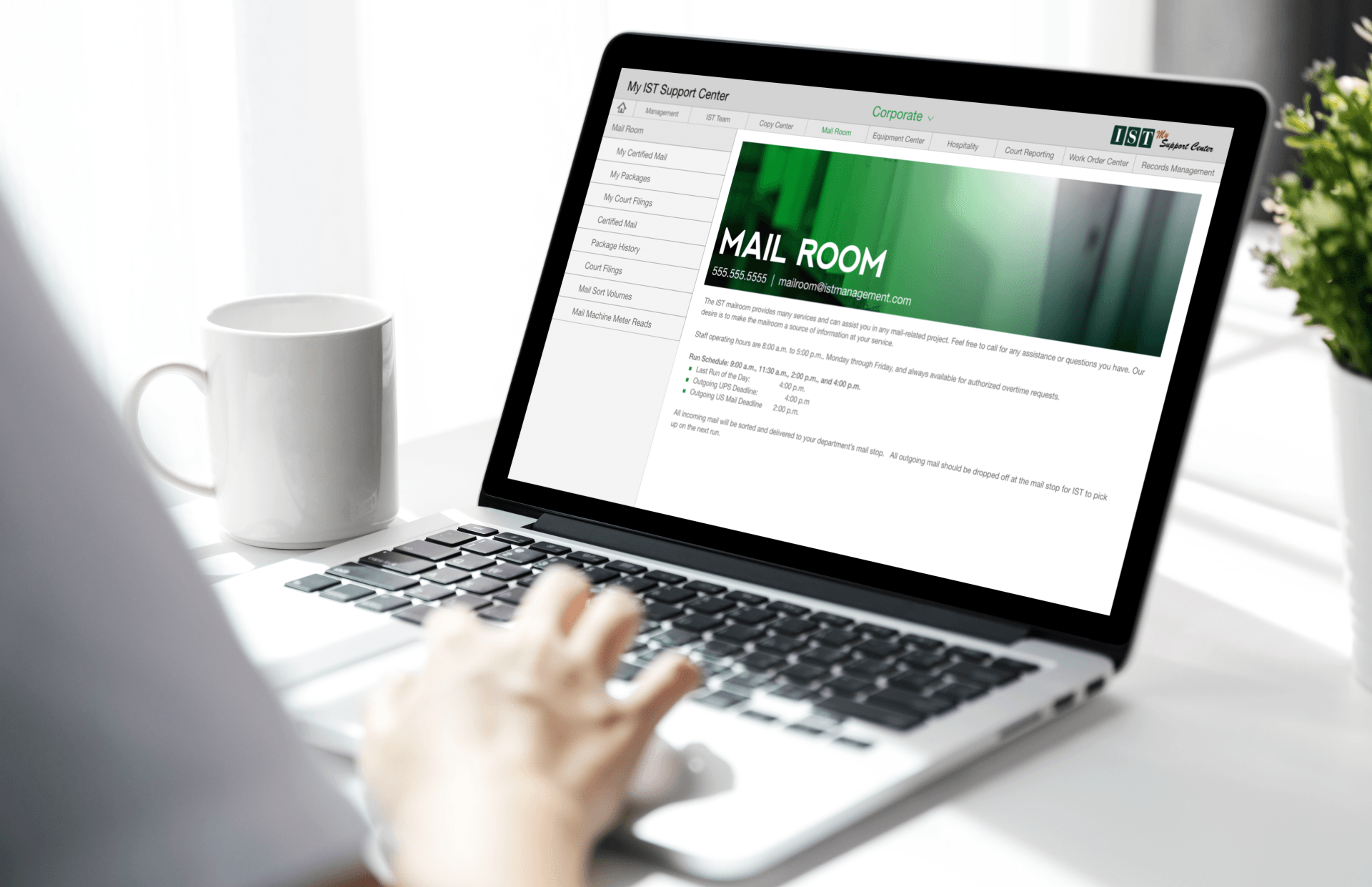 Person using a laptop on a white desk beside a mug, with a website open on screen