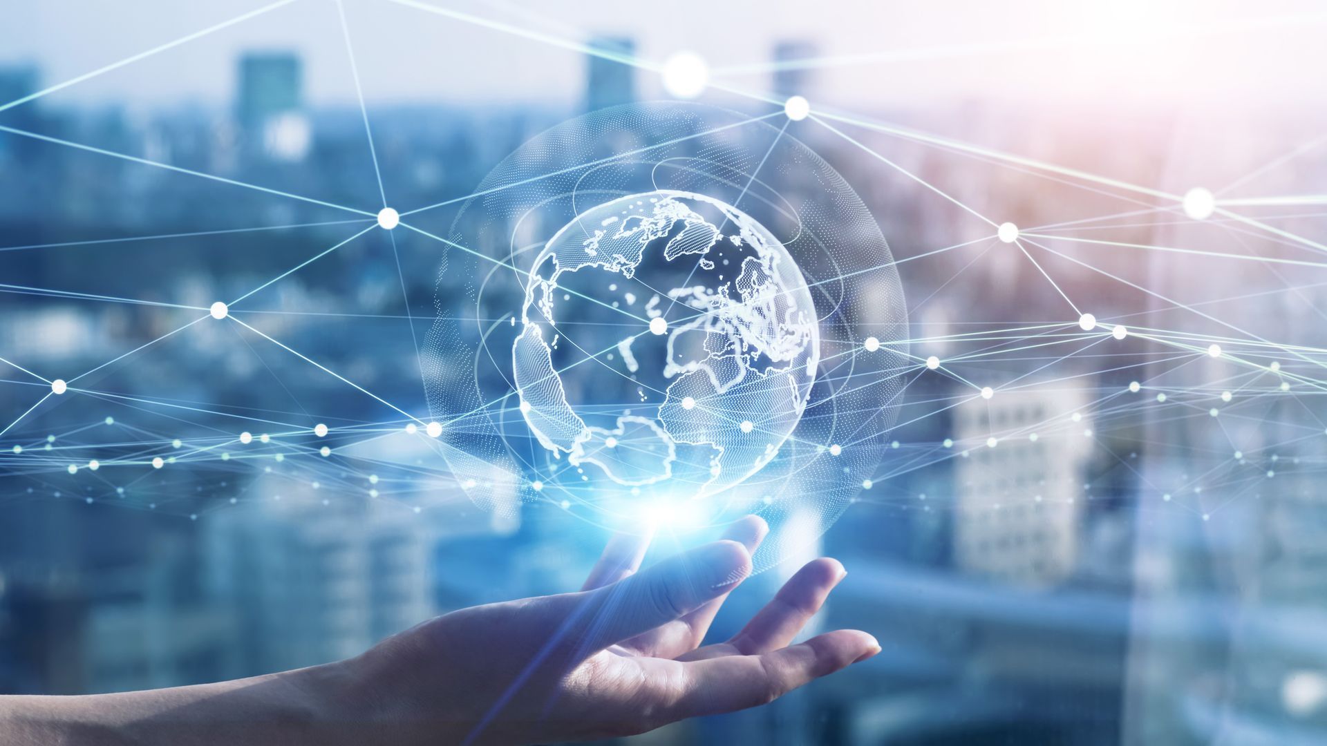 Hand holding a glowing digital globe over a blurred cityscape with network lines in the background