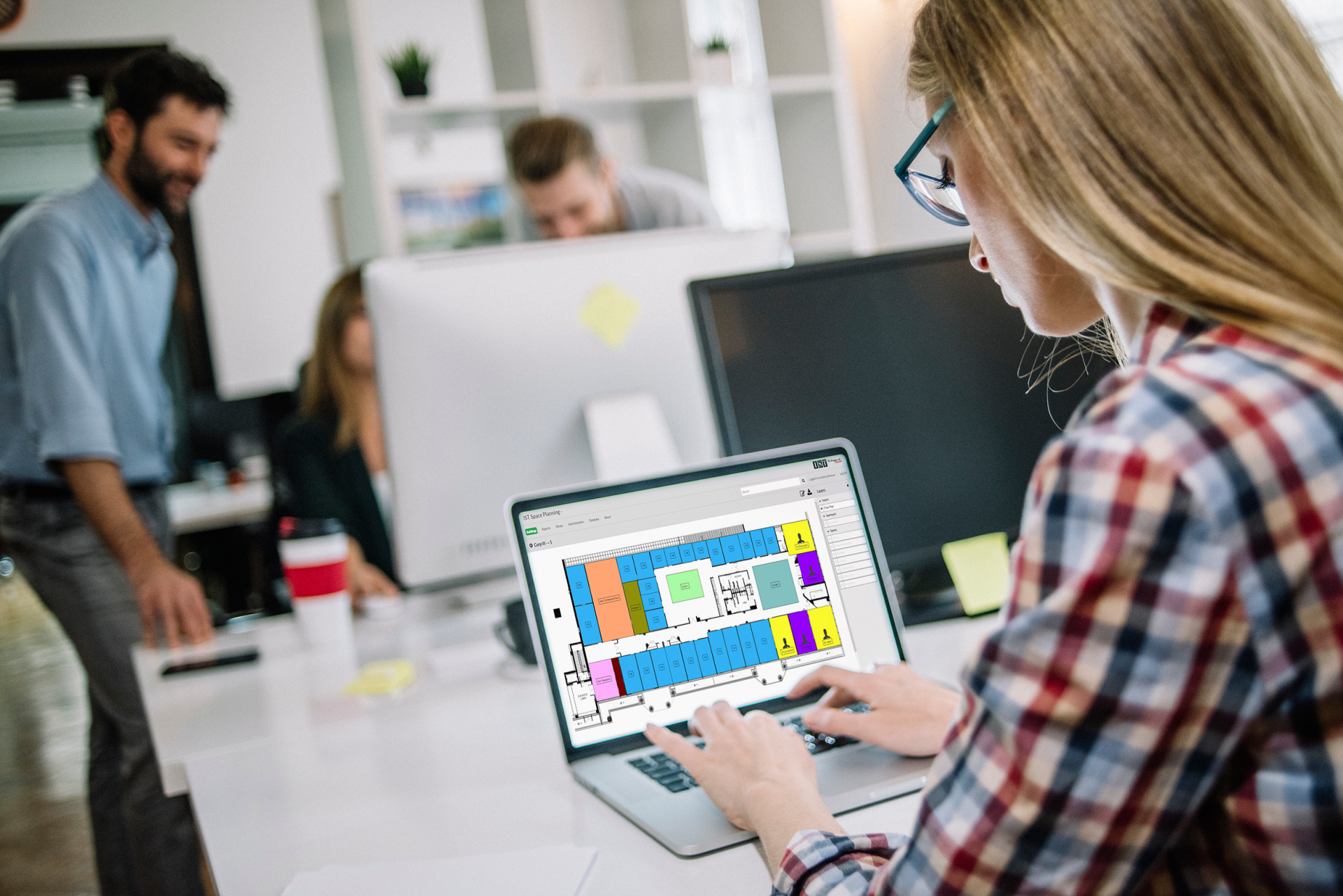 Person using a laptop in an office, viewing a colorful design layout on the screen.