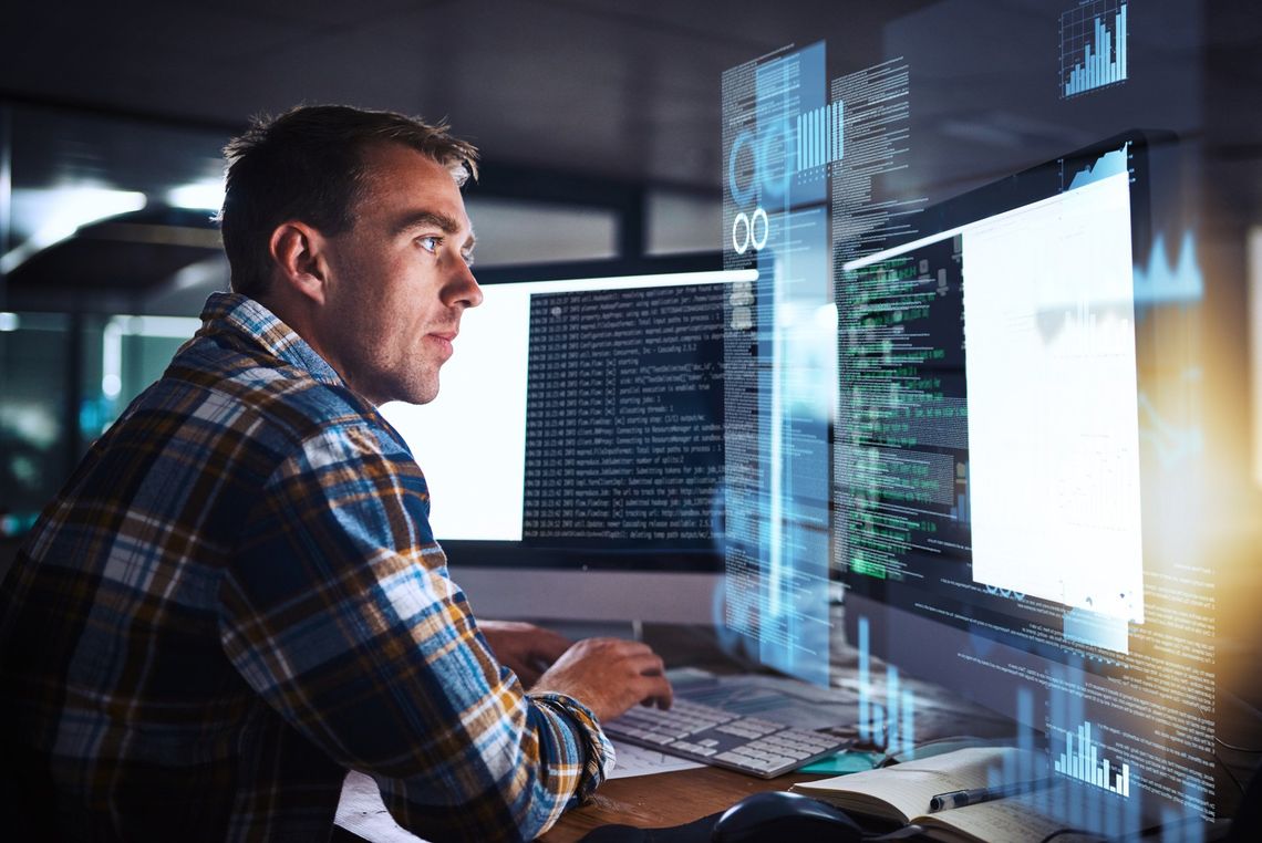 Person working at a computer with multiple glowing code screens in a dark office