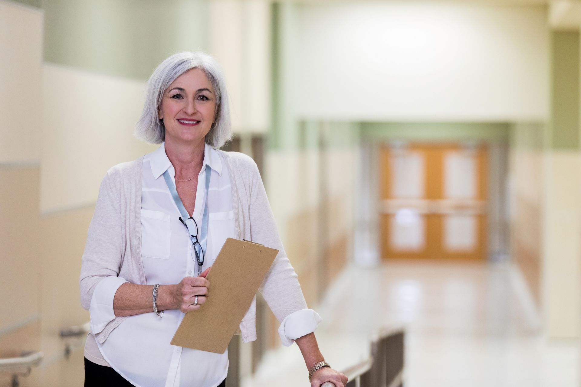 Smiling university staff member in a white blouse holding a clipboard in a bright hallway
