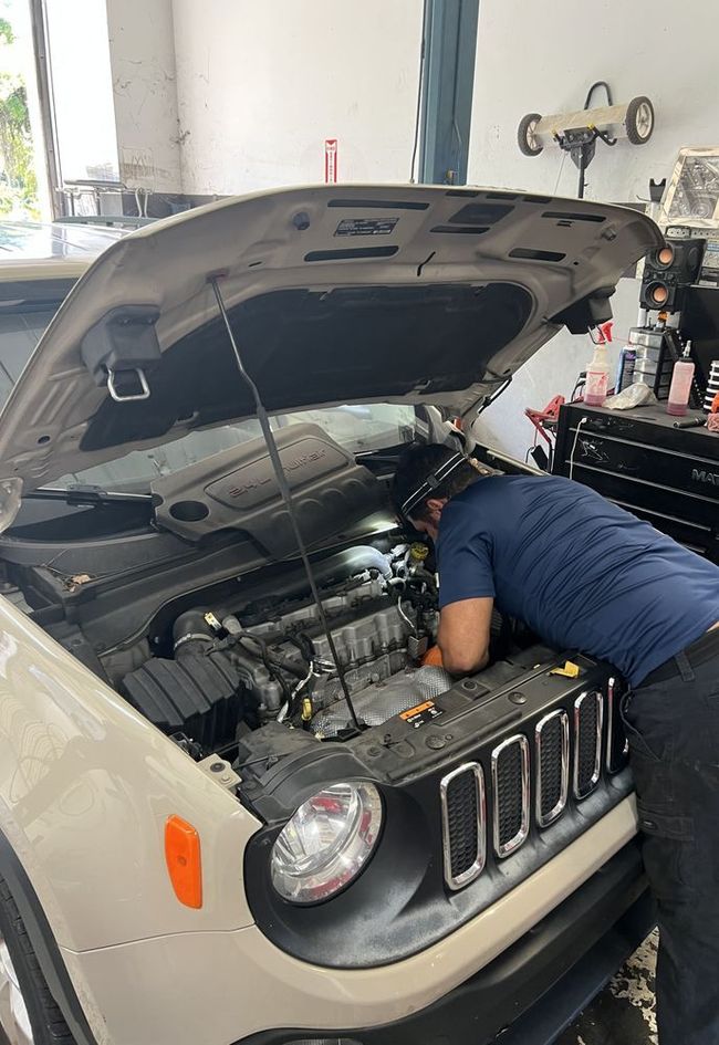 Mechanic working under the hood of a silver Jeep in a garage