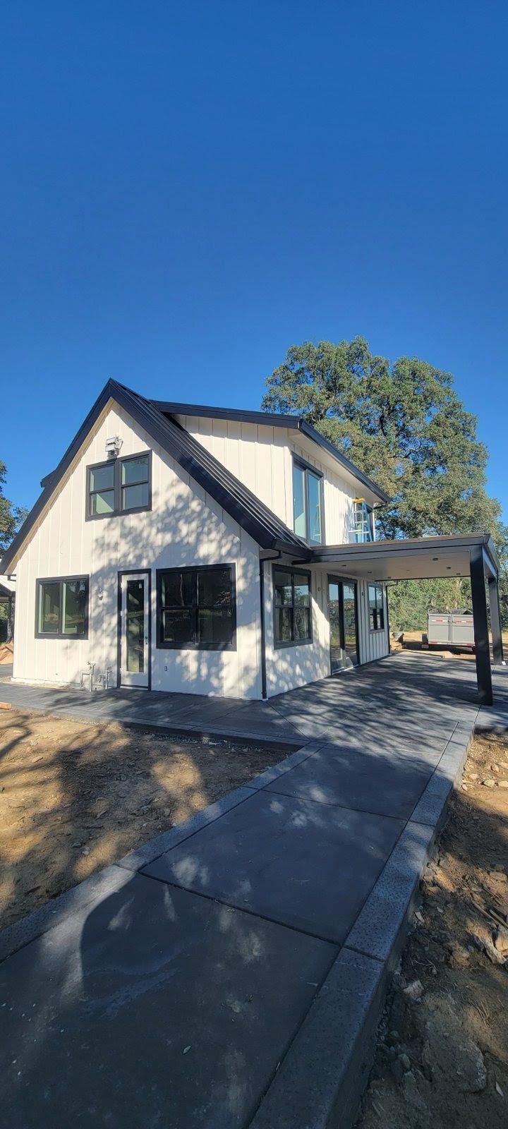 Modern white house with black trim and porch, viewed from a sidewalk on a sunny day