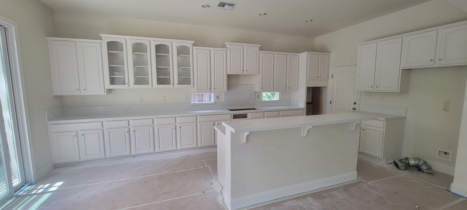Bright white kitchen with cabinets, island, and countertop in an unfinished room