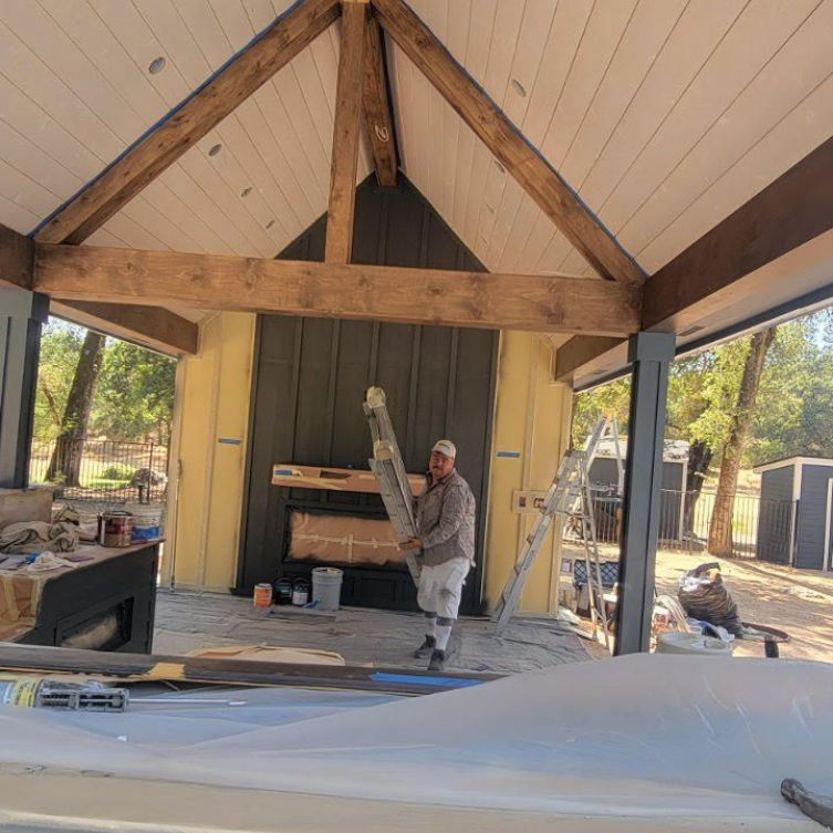 Worker on a ladder under a vaulted porch ceiling during construction or renovation.