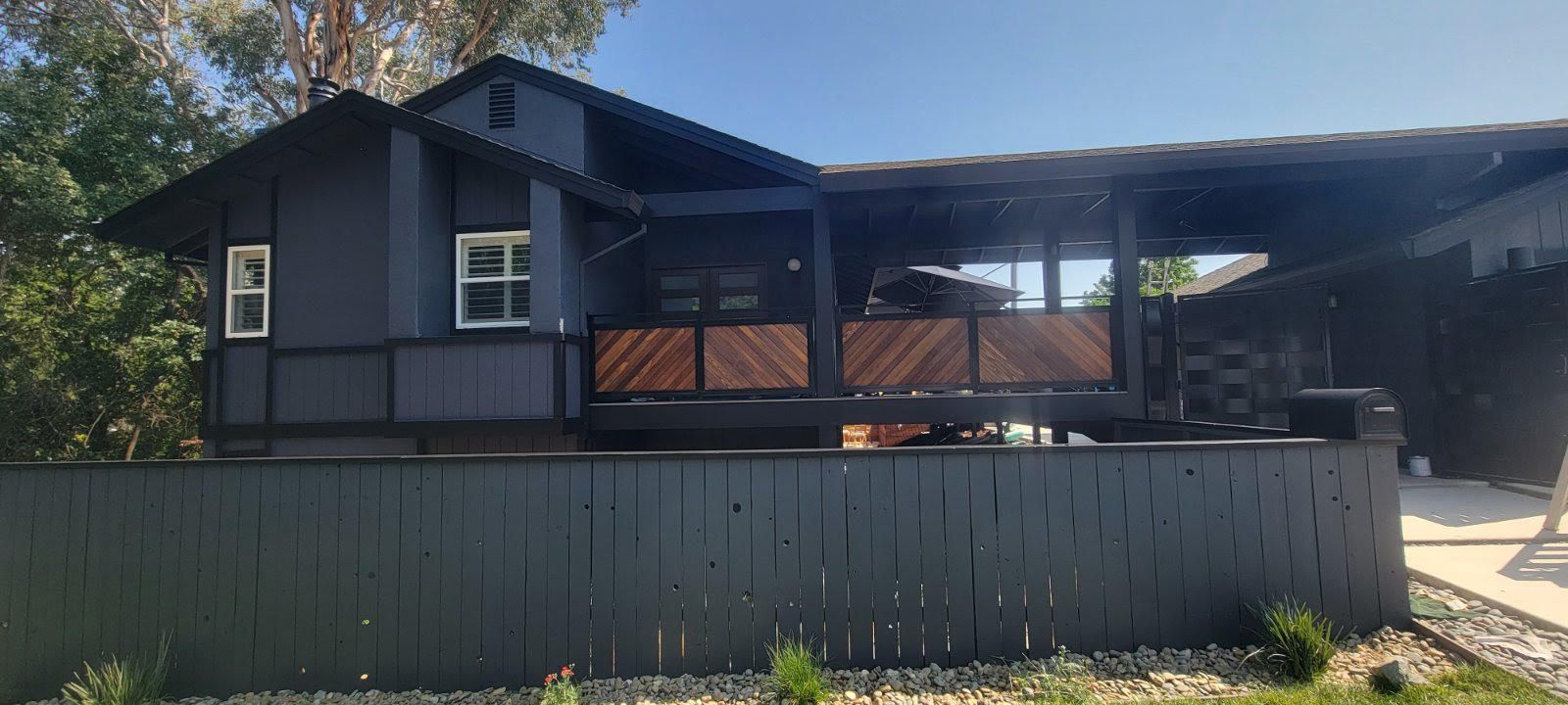 Dark blue house with a covered porch behind a gray fence on a sunny day