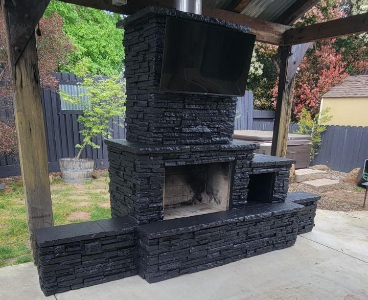 Black outdoor brick barbecue fireplace under a wooden shelter in a backyard