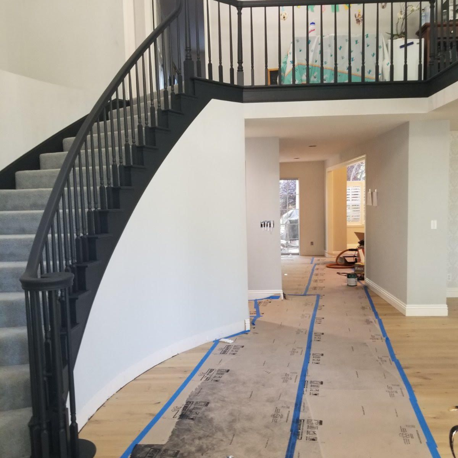 Curved black staircase in a bright foyer with taped-off flooring and white walls