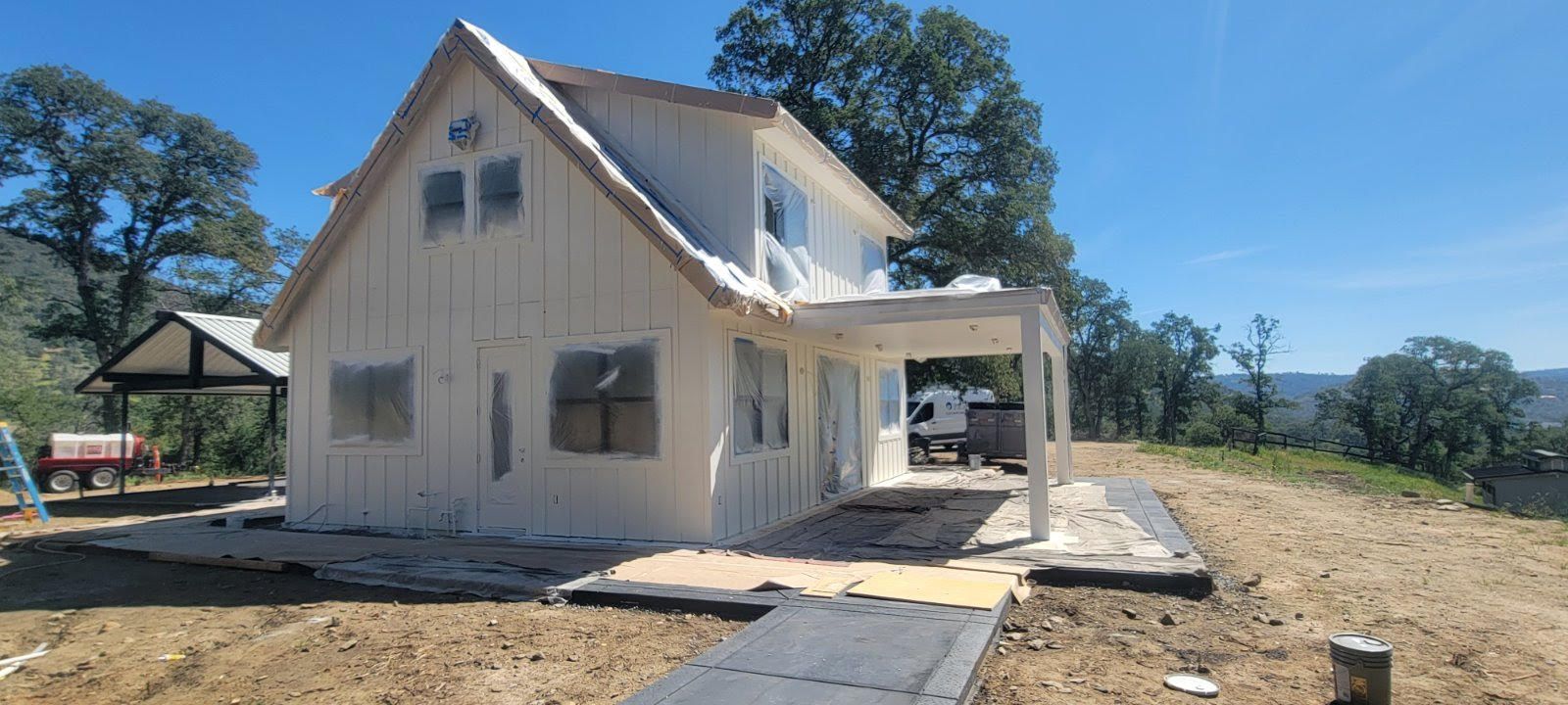 White two-story house under construction on a sunny dirt lot with a front porch and mountains in the background