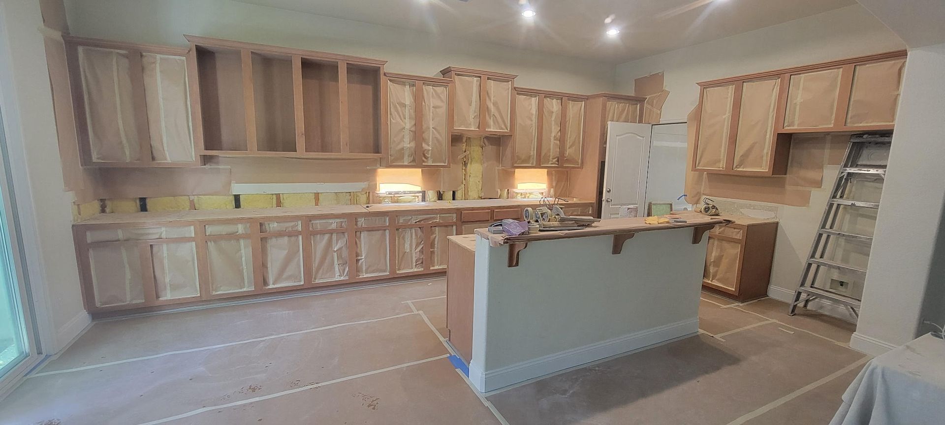 Wide kitchen under renovation with light wood cabinets, white island, and recessed ceiling lights
