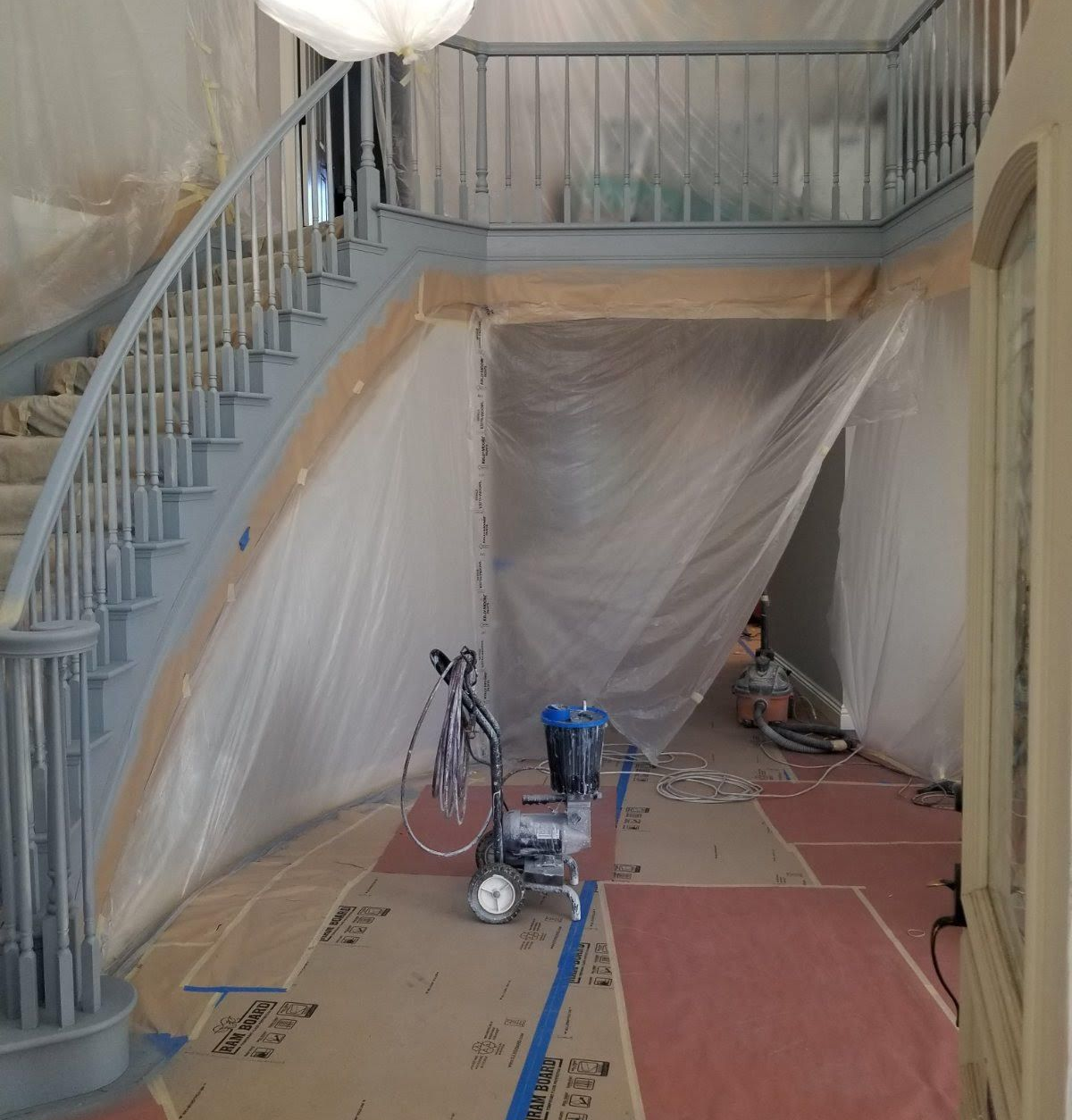 Stairwell under renovation, with plastic sheeting, tools, and protective floor coverings.
