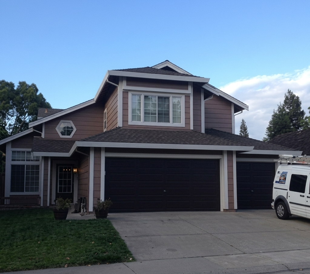 A two-story brown house with white trim and black garage doors.
