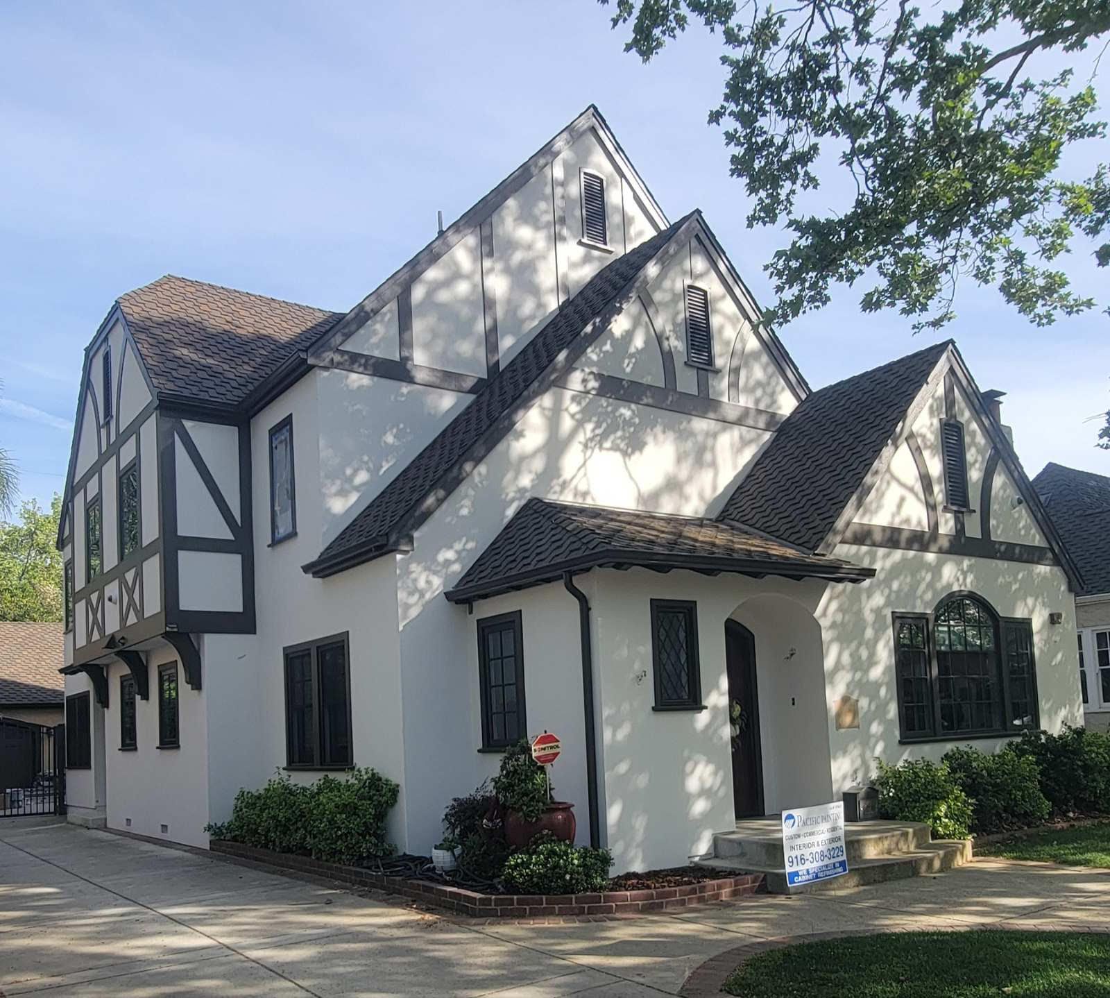 White Tudor-style house with black trim, steep roofs, and a sunlit front garden